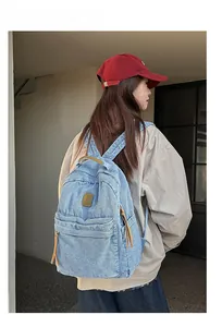 Outdoor shot of light blue denim backpack showing back view and brown leather handle strap