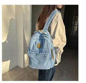 Detail of light blue denim backpack with leather logo patch and metal zipper pull