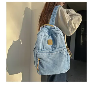 Macro detail of a light blue denim backpack showing leather pullers and brand patch