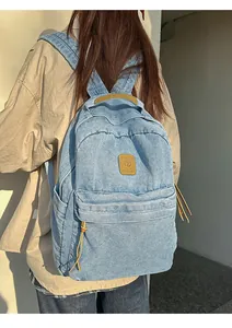 Detailed view of light blue denim backpack with brown leather strap and side pocket