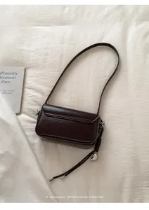 Detailopname van een donkerbruine lederen tas met zilveren hartje en gevlochten riempje