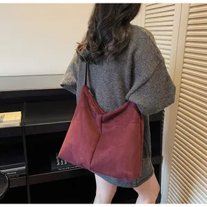 Vue latérale d'un grand sac hobo bordeaux en similicuir suédé porté par un mannequin