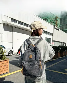Detailed view of gray washed denim backpack with leather logo patch on a 165cm model