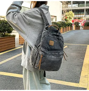 Close-up of charcoal denim backpack with brown leather accents in urban street setting