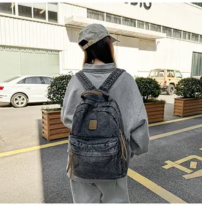 Detail of washed grey denim backpack with leather patch shown in a street scene
