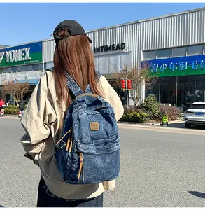 Detailed view of dark blue washed denim backpack with brown leather zipper and handle
