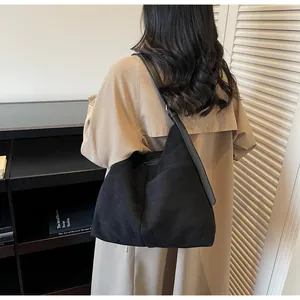 Détail du sac hobo en daim noir porté par un mannequin en manteau beige, vue de dos