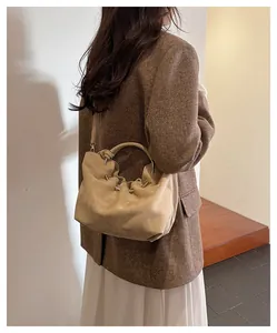 Detail of beige suede cloud bag with metal ring handle and shoulder strap on model