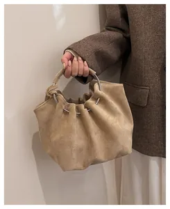 Detail of beige suede cloud bag featuring elegant pleated design and silver metal ring handles