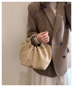 Close-up of beige suede cloud bag featuring pleated design and metal ring detail