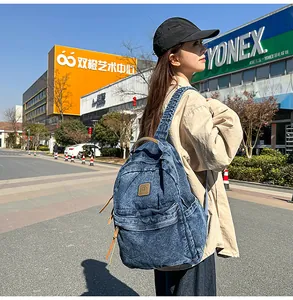 Detail of blue denim backpack with brown leather accents and brand logo on front pocket