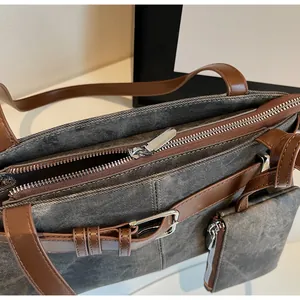 Detailopname van grijze denim tas met bruine lederen riemen en zilveren ritssluiting