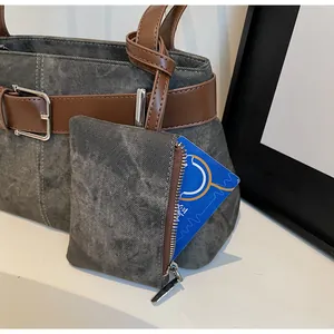Detail van grijze denim handtas met bruine leren riemen en een klein muntzakje