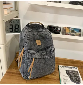 Close-up of vintage denim backpack with brown leather logo and zipper pulls on a wooden desk
