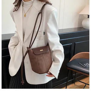 Model wearing dark brown matte leather crossbody bucket bag with gold metal trim
