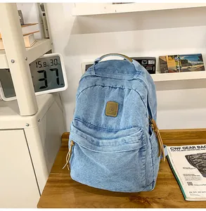 Detail of blue denim backpack showing front zip pocket and brown leather brand patch