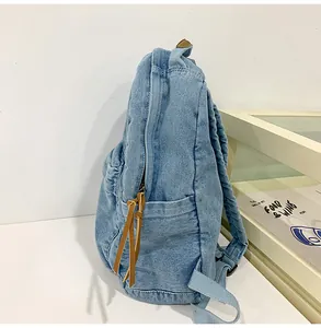 Detail view of washed denim backpack featuring side pocket and brown leather pullers