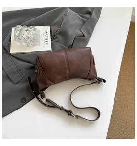 Brown faux leather dumpling bag detail with matte texture on a grey suit and art book