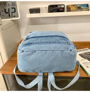 Detail of light blue denim backpack with adjustable straps on a rustic wooden desk