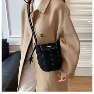 Detail of black canvas bucket bag with white stitching and gold buckle on a coat