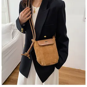 Detail of camel suede crossbody bag with fine stitching and gold metal clasp on model