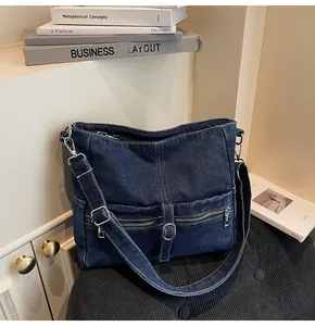 Detail of dark blue denim crossbody bag featuring outer zipper pockets and metal buckles