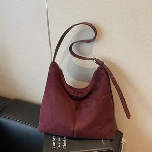 Sac hobo en daim bordeaux avec bandoulière réglable posé sur un canapé en cuir
