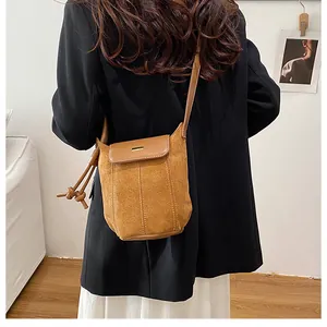 Detail of a brown suede crossbody bag with gold metal trim and decorative stitching