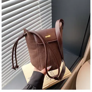 Close-up of brown suede and leather bucket bag with gold hardware and white stitching