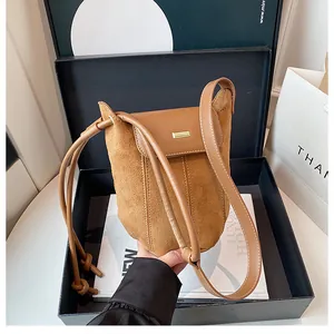 Close-up of brown suede bucket bag with gold buckle in luxury gift box packaging
