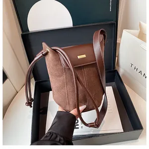 Detail of a brown bucket bag showing suede contrast stitching and gold metal plate