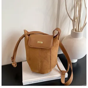 Caramel suede bucket bag on white books with minimalist gold plate detail and knot strap