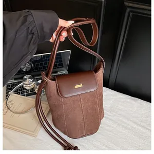 Detail of brown suede bucket bag with leather flap and gold clasp in office setting
