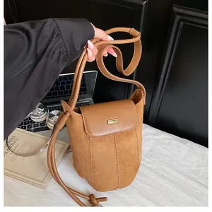 Detail of a brown bucket bag with mixed textures, suede body, and a golden metal buckle