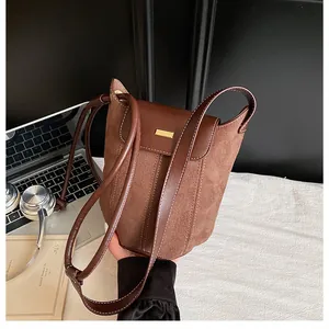 Detail of a brown suede and leather bucket bag with white stitching and gold hardware