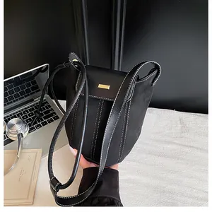 Detail of black bucket bag featuring contrast stitching and gold buckle in lifestyle setting