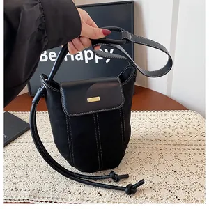 Detail of black bucket bag with contrast stitching and golden hardware on leather flap