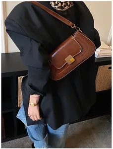 Detail einer braunen Vintage-Ledertasche mit goldener Metallschnalle auf schwarzem Blazer