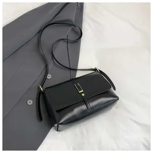 Detail of a black leather crossbody bag featuring a gold buckle and adjustable shoulder strap