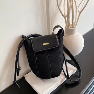 Minimalist black bucket shoulder bag featuring suede texture and contrast white stitching