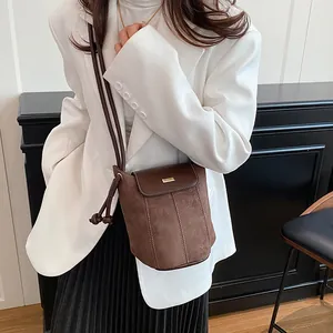 Women's dark brown suede bucket bag with gold metal trim shown on a white blazer outfit