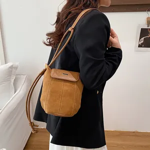 Minimalist brown suede bucket bag with leather trim worn by a model in a cozy room