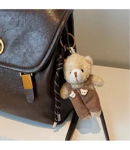 Close-up of a cute plush bear charm with corduroy overalls on a textured leather backpack