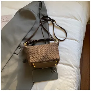 Detail view of woven dark brown crossbody bag with gold studs on a suit background