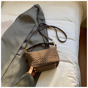 Detail of dark coffee woven leather handbag with gold hardware on white bedding