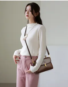 Detail of a brown lychee pattern leather crossbody bag with a gold metal lock on a model