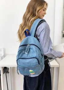 Détail d'un mini sac à dos en denim bleu clair avec broderie arc-en-ciel et sangles bleu marine