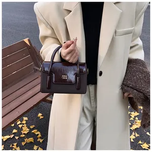 Deep brown square handbag detail featuring glossy flap and textured matte leather body