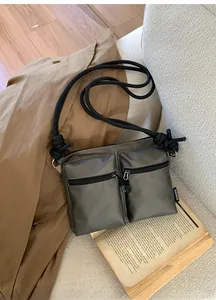 Detail of dark gray matte leather tote bag featuring dual front zipper pockets and rope strap