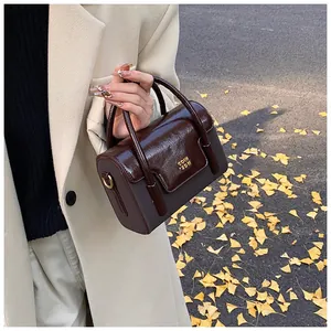 Detail view of a vintage dark brown leather crossbody bag with golden logo on beige coat